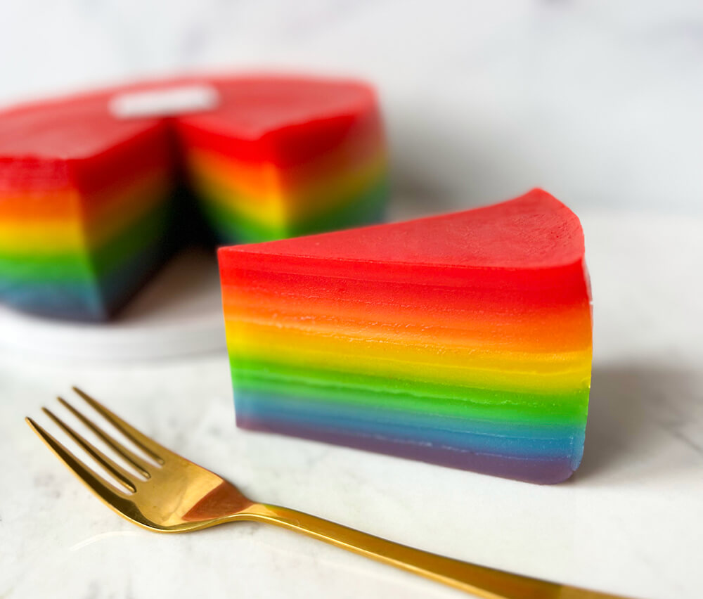 A slice of Indonesian steamed rainbow cake next to a golden fork