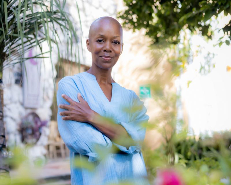 Tracye Warfield, a Black woman with a shaved head, standing in a garden