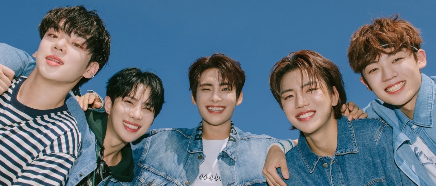 The five members of Kpop group A.C.E. standing together and smiling against a blue sky